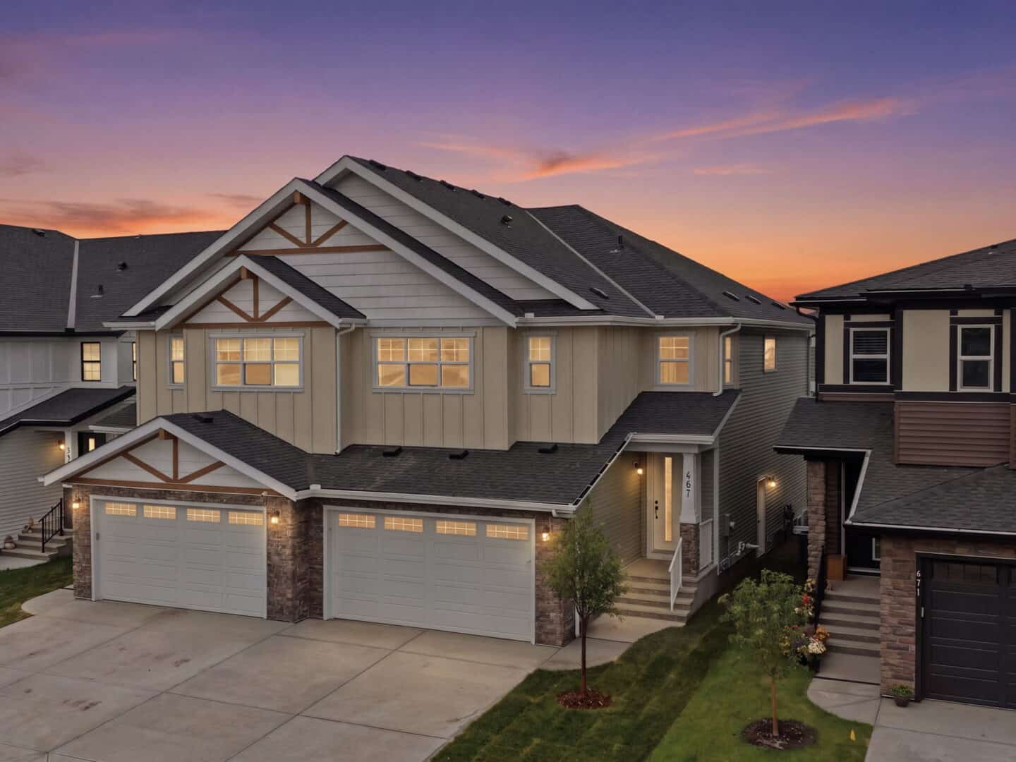 Row of modern townhouses with attached garages and gabled roofs at sunset, windows lit.